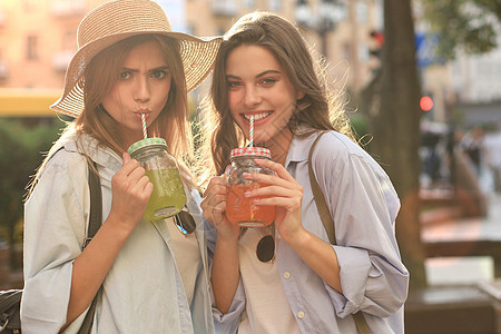 两个穿着暑期服装的美丽微笑的年轻女子 在城里玩得很开心 喝着新鲜鸡尾酒 可爱的 时尚图片