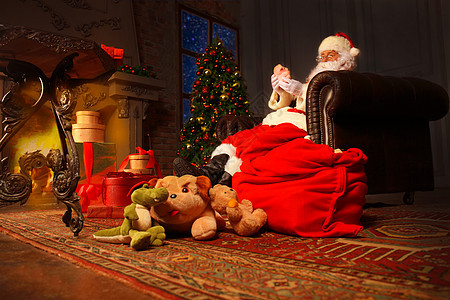 快乐圣诞老人的画像坐在他在家里的房间里靠近圣诞树 阅读圣诞信或愿望清单 成人 心愿单背景图片