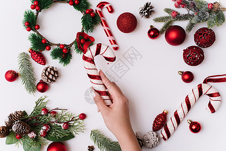 一只留着白色指甲的女性手拿着一根白色背景的甘蔗 上面有圣诞树枝和红色装饰品图片