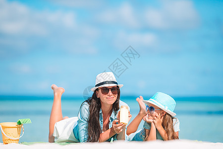年轻母亲在沙滩上给女儿鼻子涂防晒霜 保护太阳 微笑 健康图片