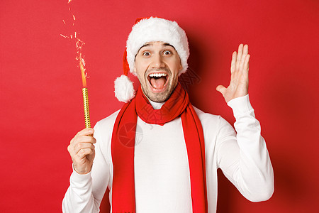 圣诞节 寒假和庆祝活动的概念 帅哥庆祝新年玩得开心 拿着烟火微笑 戴着圣诞帽 站在红色背景上 庆典 美丽的图片