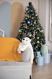 圣诞树上有蓝色和金色的玩具 客厅里的圣诞树 装饰着蓝色饰品和花环 树下有很多礼物 冰熊在椅子上 冬季假期图片