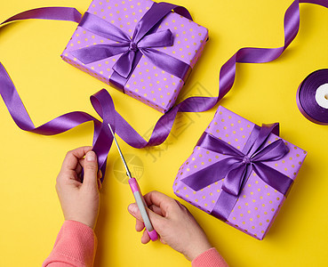 女性手正在剪裁一个丝绸紫色丝带 带有剪刀 紧靠礼品盒图片