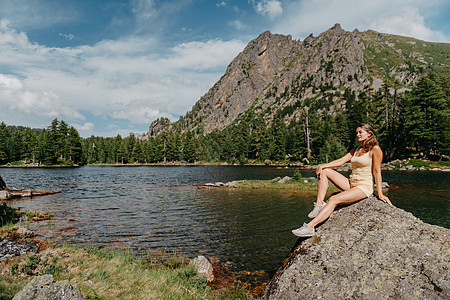 旅游女孩喜欢坐在山上绿松石湖岸边的大石头上欣赏湖泊 针叶林和神奇景色的神奇景色 在自然公园徒步旅行 可爱的女孩游客坐在湖边的一块图片