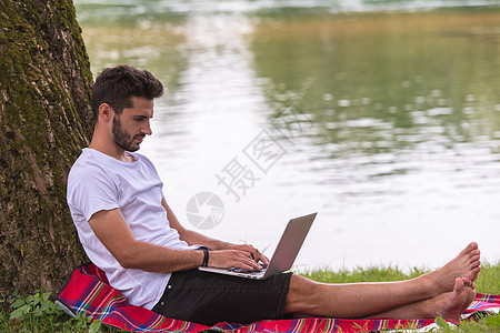 在河岸上使用笔记本电脑的男子 假期 网络 公园图片