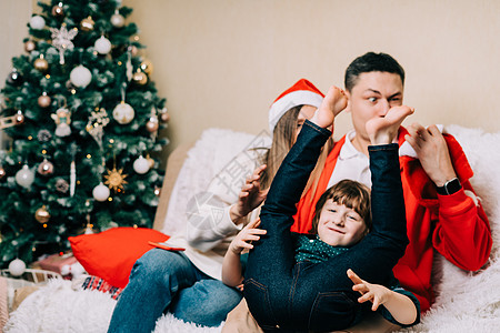 快乐微笑的家庭和孩子的儿子玩得开心和傻瓜 戴着圣诞帽的笑妈妈 爸爸 穿着毛衣的小男孩在家里过圣诞假期玩得很开心 圣诞快乐和新年快图片