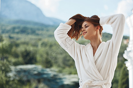 穿着白色浴袍的漂亮女人长发留在酒店的阳台上 完美的阳光明媚的早晨 喝 夏天图片