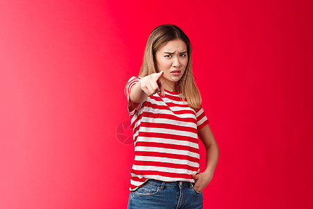 姑娘请你认罪 心烦意乱的亚洲金发女友被指着相机欺骗指责人指责 皱着眉头失望和受伤 站在红色背景上被冒犯 咧着嘴笑 抱怨图片