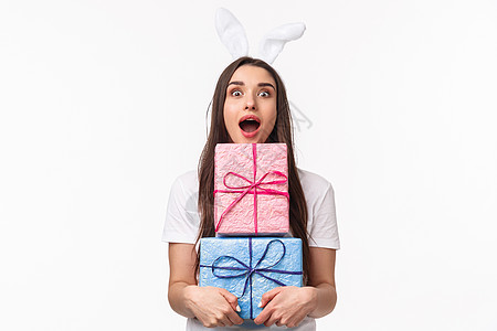 庆祝活动 假期和礼物的概念 有趣的年轻漂亮女人的画像 长着兔子耳朵 张着嘴兴奋 拿着一包礼物 收到很棒的礼物 白色背景 女性 头图片