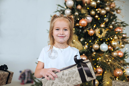 迷人的小女孩拿着礼物 在圣诞树背景上做着圣诞树的背景 幸福 庆典图片