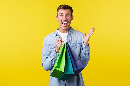 购物 休闲和折扣概念 兴奋的英俊微笑男人高兴地尖叫着从商店提着特价商品的袋子 对优惠的价格 黄色背景做出惊讶的反应图片