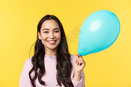 人们的情感 生活方式的休闲和美容理念 可爱的微笑亚洲女孩拿着蓝色气球祝贺大型活动 站在黄色背景 参加惊喜派对图片