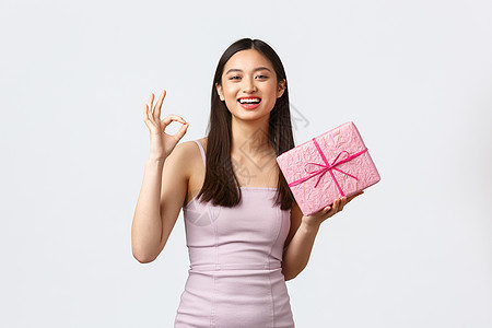 庆典 聚会和假期的概念 穿着晚礼服 拿着生日礼物 包裹着礼物的盒子的快乐亚洲女孩 表现出好的姿态 微笑着快乐 白色背景图片