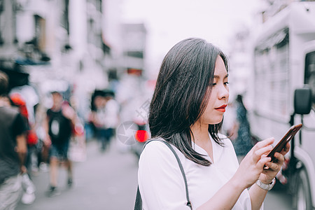 一位年轻女性在泰国曼谷著名的背包车街高山 Khao San 玩手机 市场 太阳图片