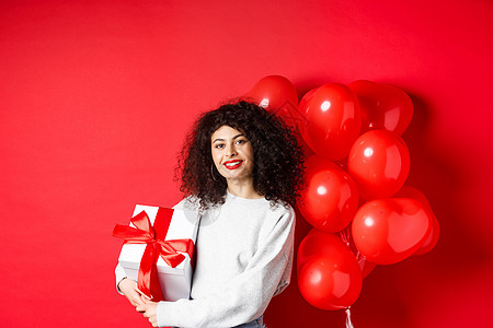 美丽的白人女性 深色卷发 红唇 拿着浪漫的心形气球站着 放在盒子里 收到情人的礼物 站在工作室的背景上 女士 男朋友图片