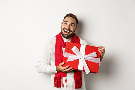 圣诞节快乐 快乐的男人看起来欣喜若狂 拿着他的新年礼物 站在白色背景下图片