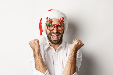 庆祝圣诞节或新年的男人的特写镜头 戴着圣诞派对眼镜和圣诞老人的帽子 欢欣鼓舞 欢呼雀跃 站在白色背景上 成人 情感图片