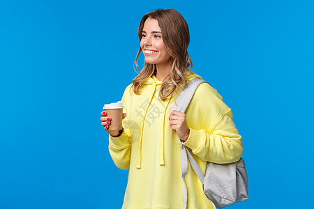 上大学时 无忧无虑的漂亮年轻女学生用纸杯喝咖啡 背着背包 带着愉快轻松的微笑 生活方式和人的观念望向一旁 喜悦 金发女郎图片