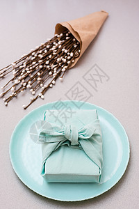环保礼物 — 一个用布包裹在盘子上的盒子和一束灰色背景的褪色柳 极简主义 垂直视图图片