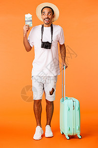 全长垂直拍摄让快乐的非洲裔美国人兴奋地梦想着假期 抬头看着有趣和想象旅行 拿着护照和机票 行李 橙色背景图片