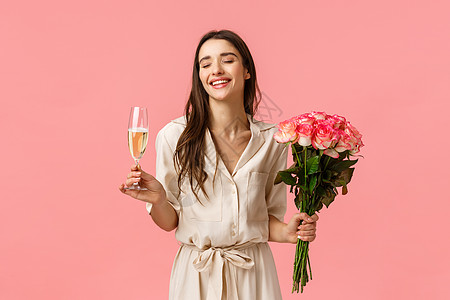 庆典 派对和美容理念 浪漫美丽的年轻女子穿着裙子 手捧鲜花享受庆祝 喝着玻璃香槟 闭上眼睛笑着 粉红色的背景图片