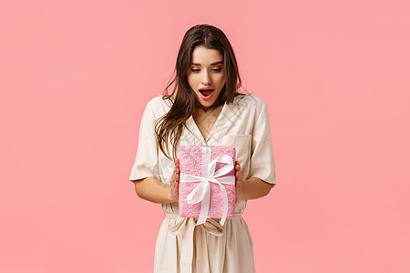 惊喜 庆祝和节假日概念 惊讶的女友拿着现物盒 没有快快地收到礼物 张开口唇迷得发狂的外表触摸着包装箱 粉红色背景背景图片
