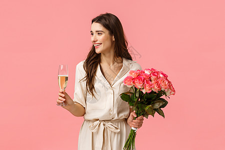 优雅 庆典和派对理念 有魅力的年轻快乐女人过生日 收到礼物 美丽的鲜花 拿着玫瑰和香槟杯 向左微笑 粉红色背景图片