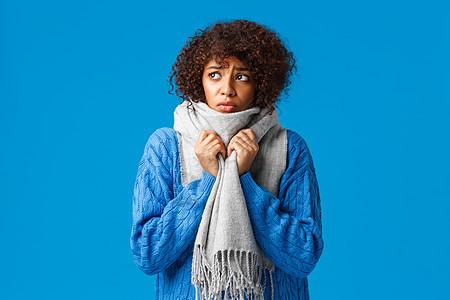 愚蠢而悲伤 阴郁的非洲裔美国女孩看着外面多风的雪天冬天 用温暖的围巾裹住脖子 因家里低温 蓝色背景而感到寒冷不适而颤抖图片
