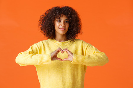 爱我本来的样子 体贴 温柔 可爱 浪漫的非洲裔美国女性表达自己的感受 展示心形 在情人节表白爱情 站在橙色背景中快乐图片