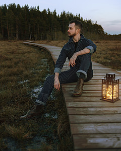 一个穿蓝制服和棕靴子的男人 坐在森林里一个木制的图片