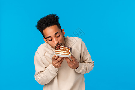 味道真好 高兴而高兴的留着胡子的非洲裔美国人喜欢甜食 参加朋友的生日聚会 咬着一块蛋糕喜欢味道 享受美食 站在蓝色背景上快乐图片
