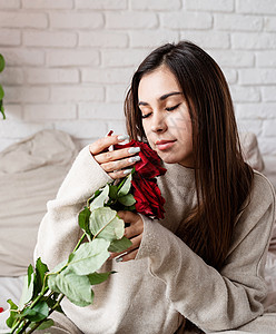 年轻美女坐在床上 庆祝情人节 盛着红玫瑰的晚礼日 假期 微笑图片