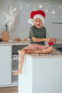 一个小男孩戴着圣诞老人帽子 喝着可可牛奶 坐在厨房桌子上图片