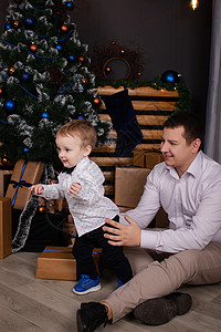 蹒跚学步的小男孩和男人在圣诞树和装饰附近 儿子和父亲在平安夜 新年 单身父亲 不完整的家庭图片
