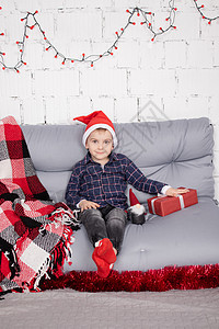戴着圣诞老人帽子的小男孩靠近圣诞侏儒玩具 在灰色的房间里手里拿着矮人玩具 圣诞装饰和玩具 孩子们玩耍 装饰风格 庆典图片