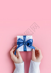 在粉红背景白包装纸上佩戴礼物的女性手 以粉红色背景图片