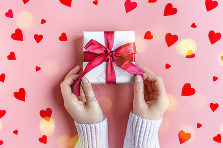 女性手拿着一件礼物 印在红心粉红背景的白包装纸上 丝带 美甲图片