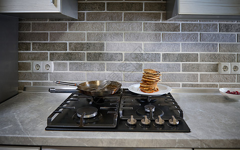 白色盘子上鲜烤自制煎饼 钢煎锅和家用厨房黑炉子上的烟片前视线 周二概念图片