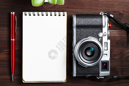 深棕色木桌上带空白记事本页和红笔的经典相机 带电话和绿花的古董桌 纸 假期图片