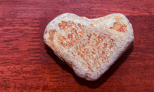 石头在红色调的木质表面上形状像一颗心 心由木制背景上的天然石材制成 情人节和假期概念 浪漫的 复古的图片