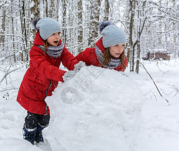 两个穿红色夹克的双胞女 滚大雪球来造雪人图片