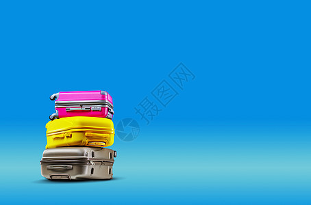 三个多色手提箱在蓝色背景下躺在彼此的顶部图片