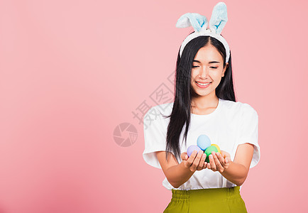 妇女笑着穿着兔子耳朵 手拿着彩色复活节鸡蛋礼物 潮人 奢华图片