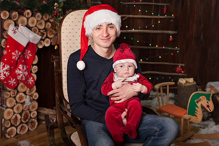 一个带着孩子的男人 打扮成圣诞老人 在椅子上 在新年前夕的木制壁炉旁 一圈 礼物图片
