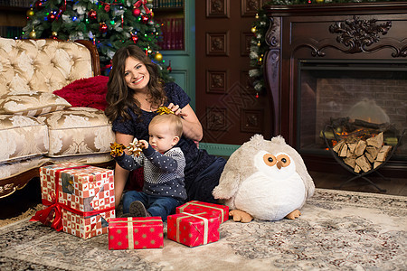 母亲和儿子在圣诞树和壁炉附近的地毯上打开圣诞礼物 传统 畅快图片
