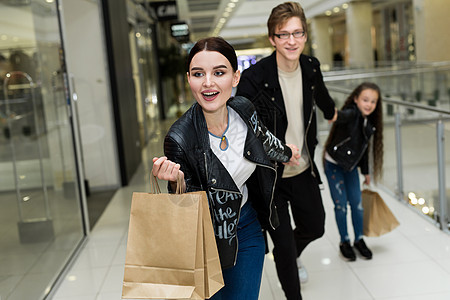 快乐的年轻家庭在购物中心买纸袋 用衣服去商店窗户 父母 购物者图片
