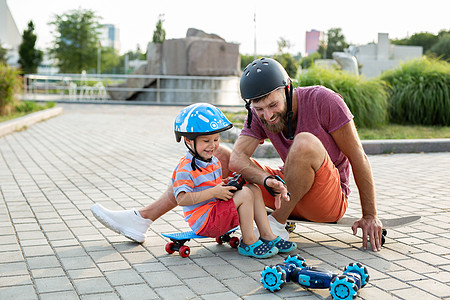 身戴头盔的快乐父亲和儿子在公园玩耍 驾驶机器人汽车 坐在滑板上时由手套控制 快乐的 粘接图片