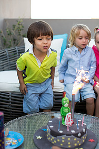 孩子们生日派对 孩子在多彩蛋糕上吹蜡烛图片