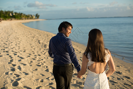 新娘和新郎在毛里求斯海滩上行走 棕榈树 吻 花束图片