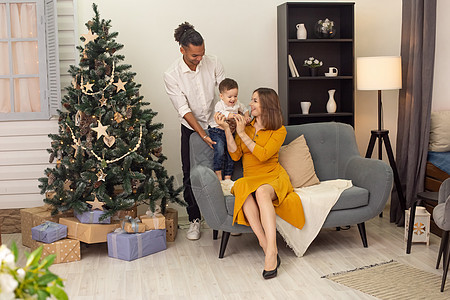 幸福的年轻家庭快乐地在家中灰色沙发上玩耍 旁边是圣诞树图片